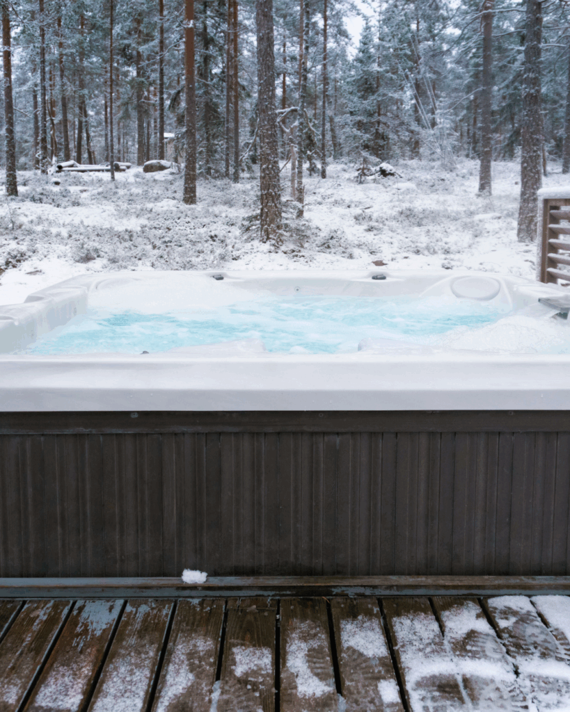 a hot tub in winter surrounded by snow in the woods.