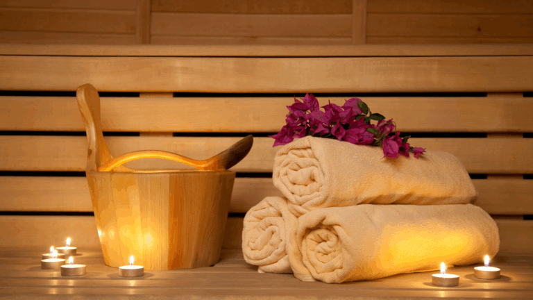 bench seat in a sauna with a bucket and water scoop as well as towels, candles and flowers.