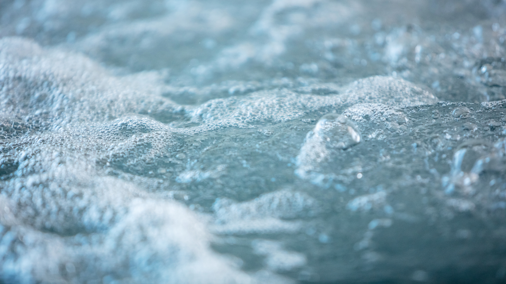 a close up photo of water in a hot tub, with small bubbled. the water is a pale blue/teal colour, and no parts of the hot tub itself are visible in the photo, just the water.