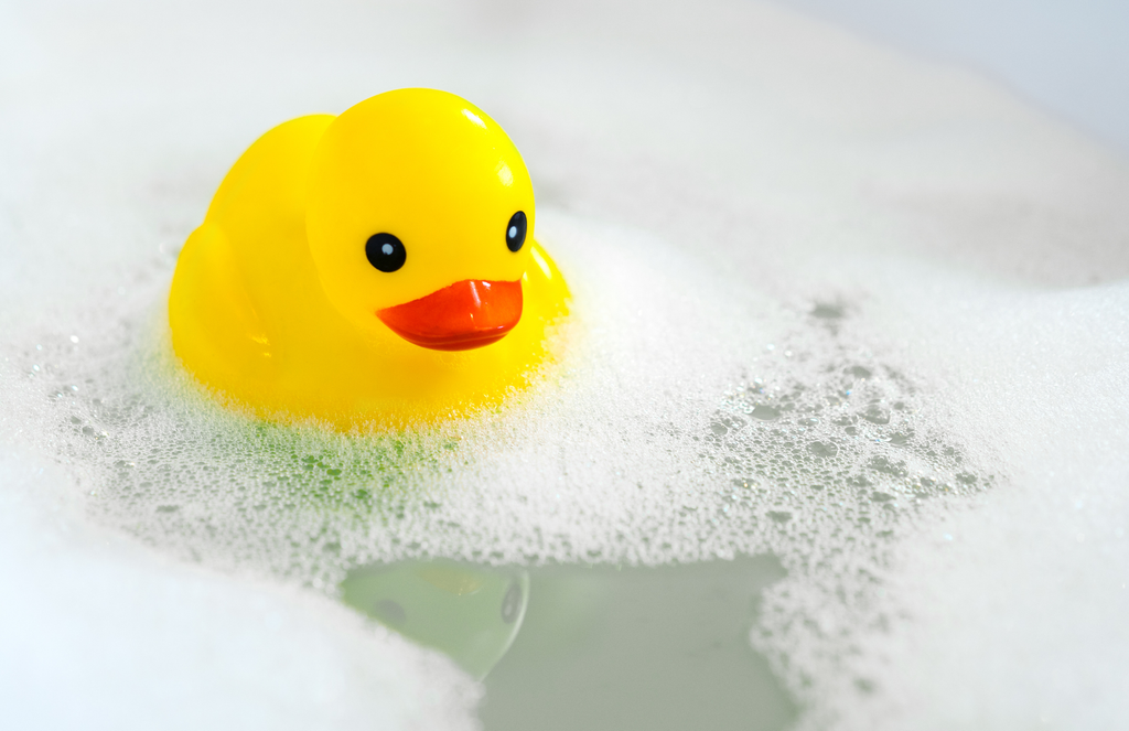 a yellow rubber duck in water that has a layer of bubbles and foam on top.